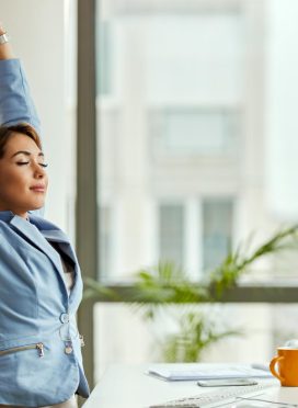 joven-mujer-negocios-sonriente-que-estira-ojos-cerrados-mientras-trabaja-computadora-oficina